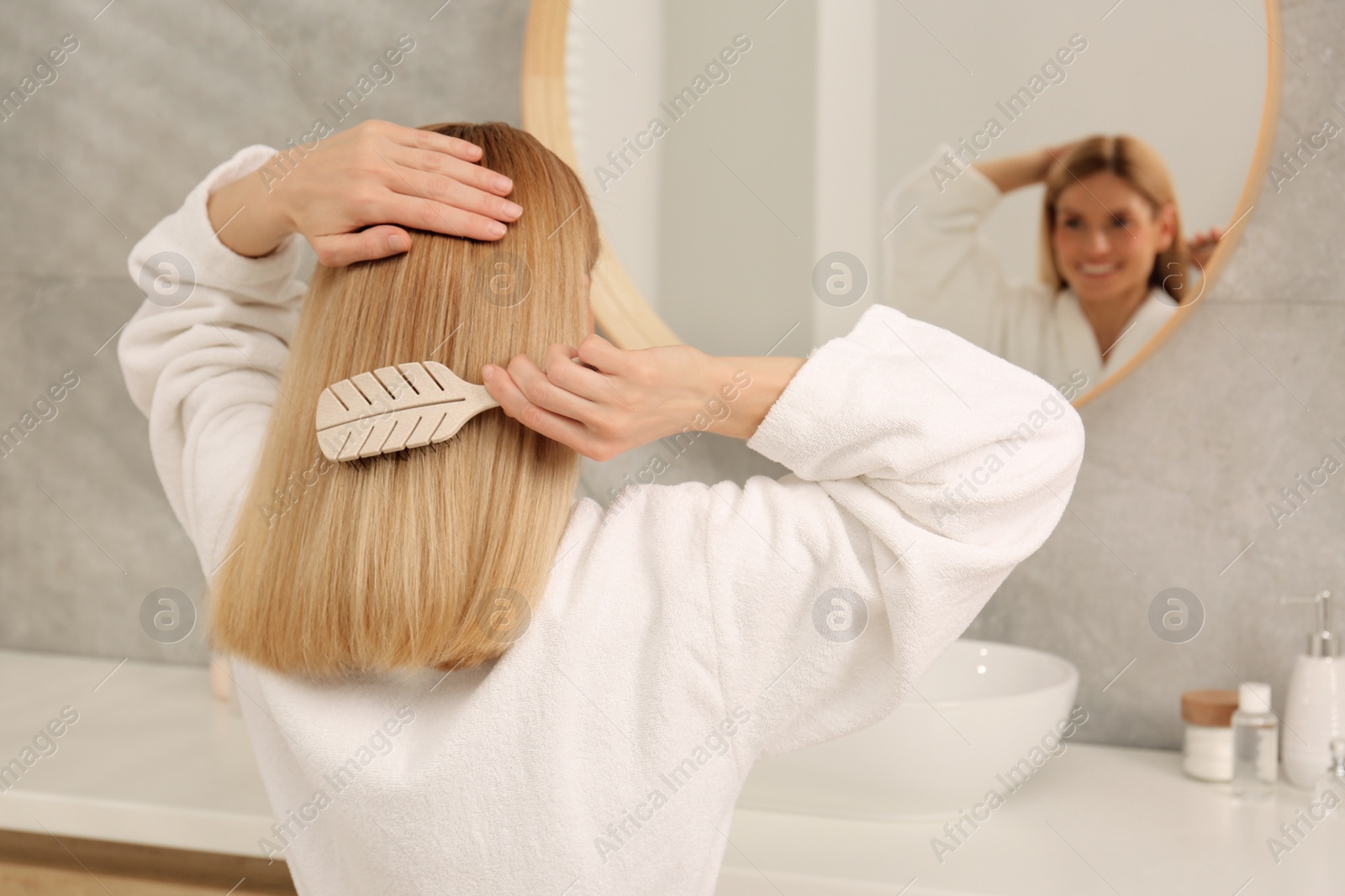 Photo of Beautiful woman brushing her hair near mirror in bathroom