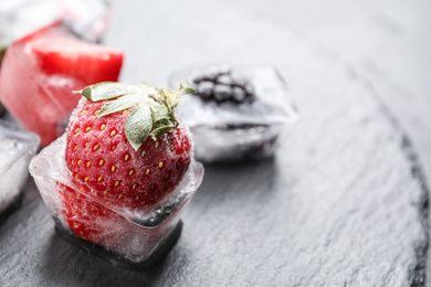 Ice cubes with different berries on dark grey table, closeup. Space for text