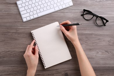 Photo of Woman writing in notebook at wooden table, top view