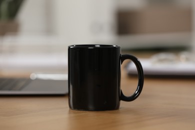 Photo of Black ceramic mug on wooden table at workplace