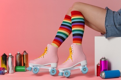 Photo of Woman with vintage roller skates and spray paint cans on color background, closeup