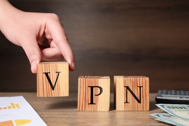 Photo of Woman making acronym VPN with cubes at wooden table, closeup