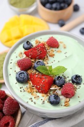 Photo of Tasty matcha smoothie bowl served with berries and oatmeal on white table, closeup. Healthy breakfast