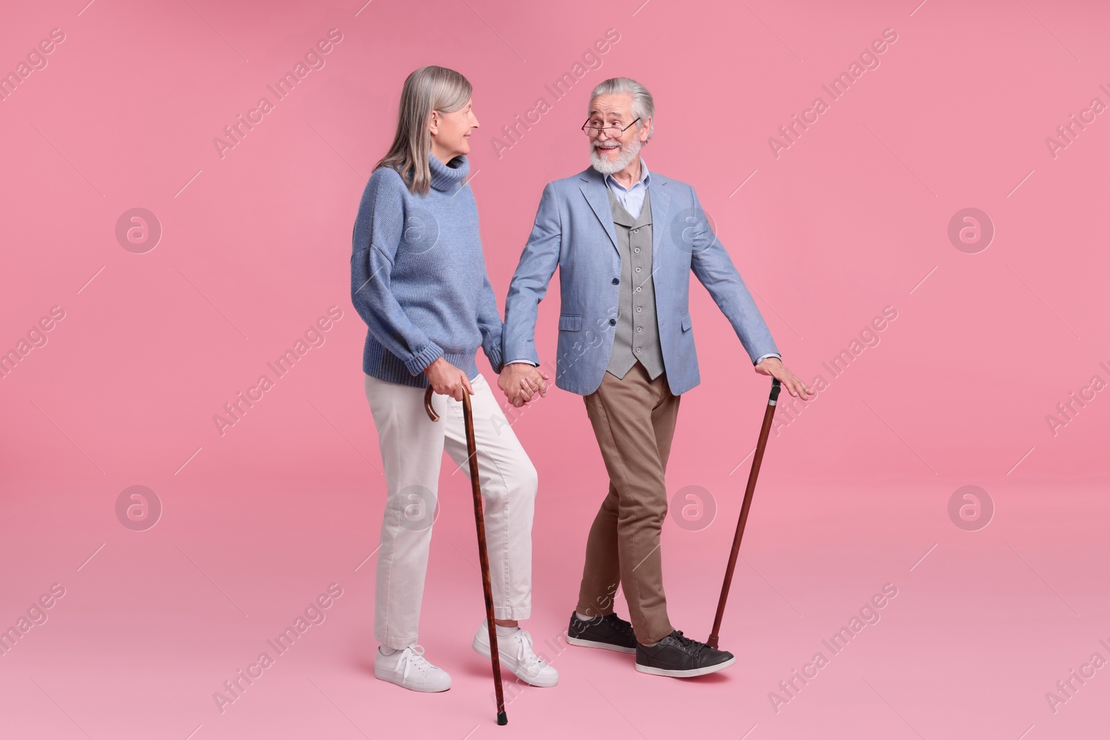 Photo of Senior man and woman with walking canes on pink background