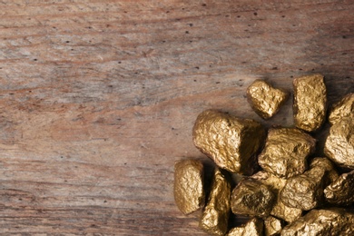 Photo of Pile of gold nuggets on wooden background, top view with space for text