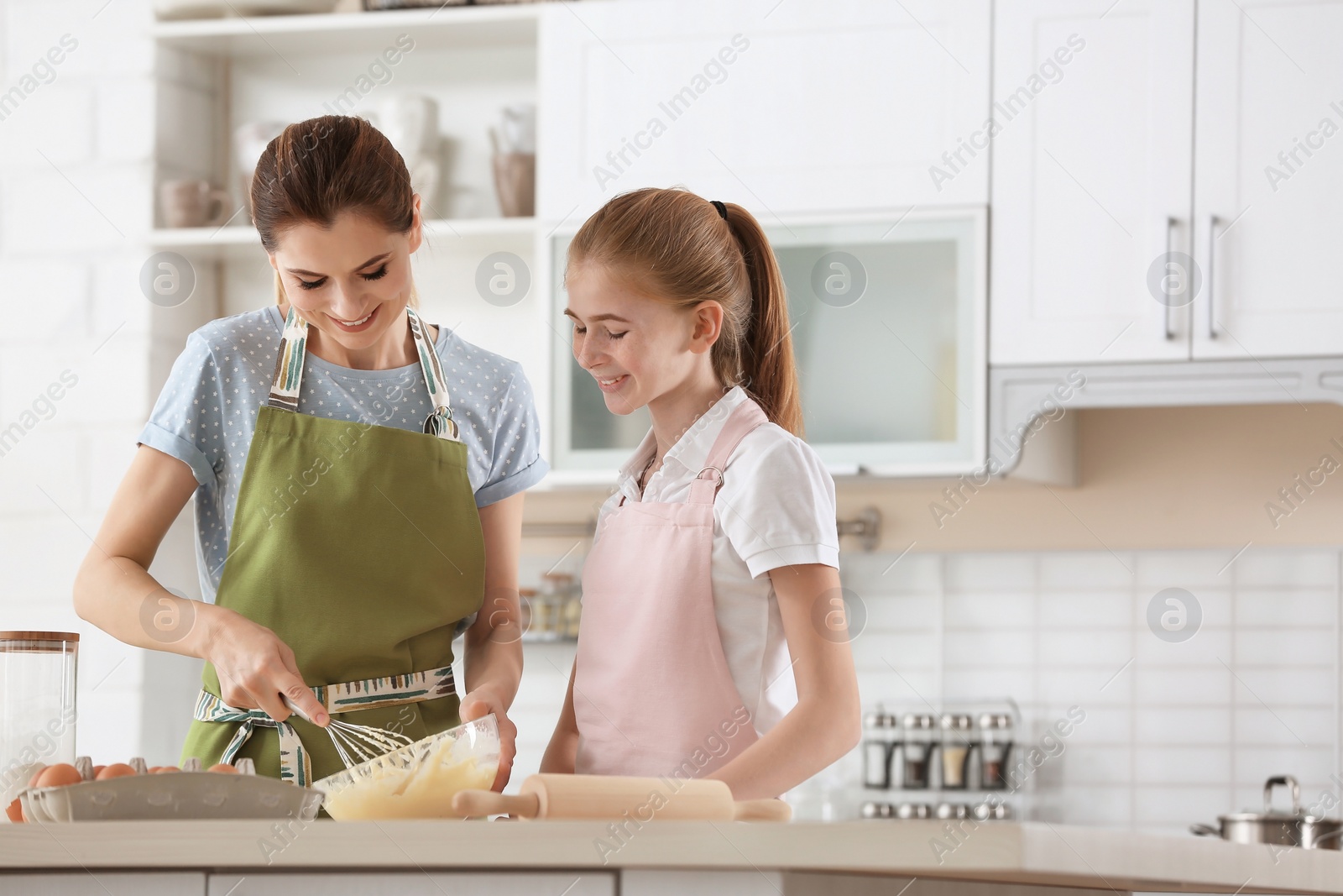 Photo of Mother and her daughter making dough at table in kitchen