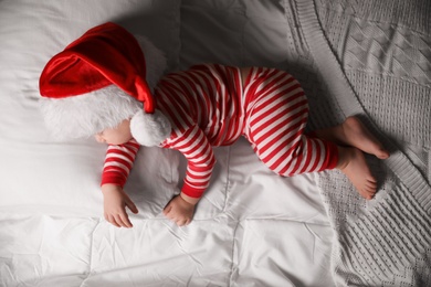 Photo of Baby in Santa hat sleeping on bed with white linens, top view
