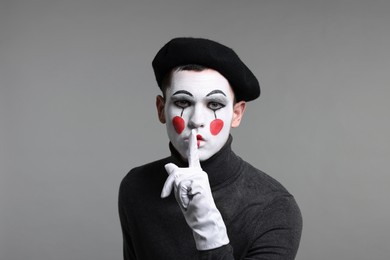 Photo of Mime artist in beret showing hush gesture on grey background