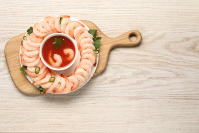 Photo of Tasty boiled shrimps with cocktail sauce, chili and parsley on light wooden table, top view. Space for text