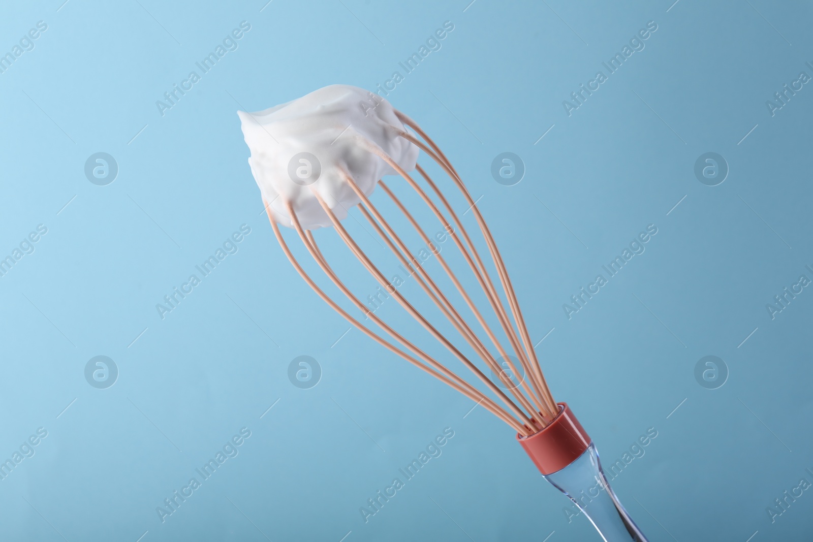 Photo of Whisk with whipped cream on light blue background