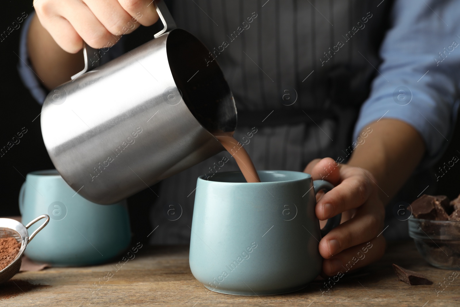 Photo of Woman pouring hot cocoa drink into cup on wooden table, closeup
