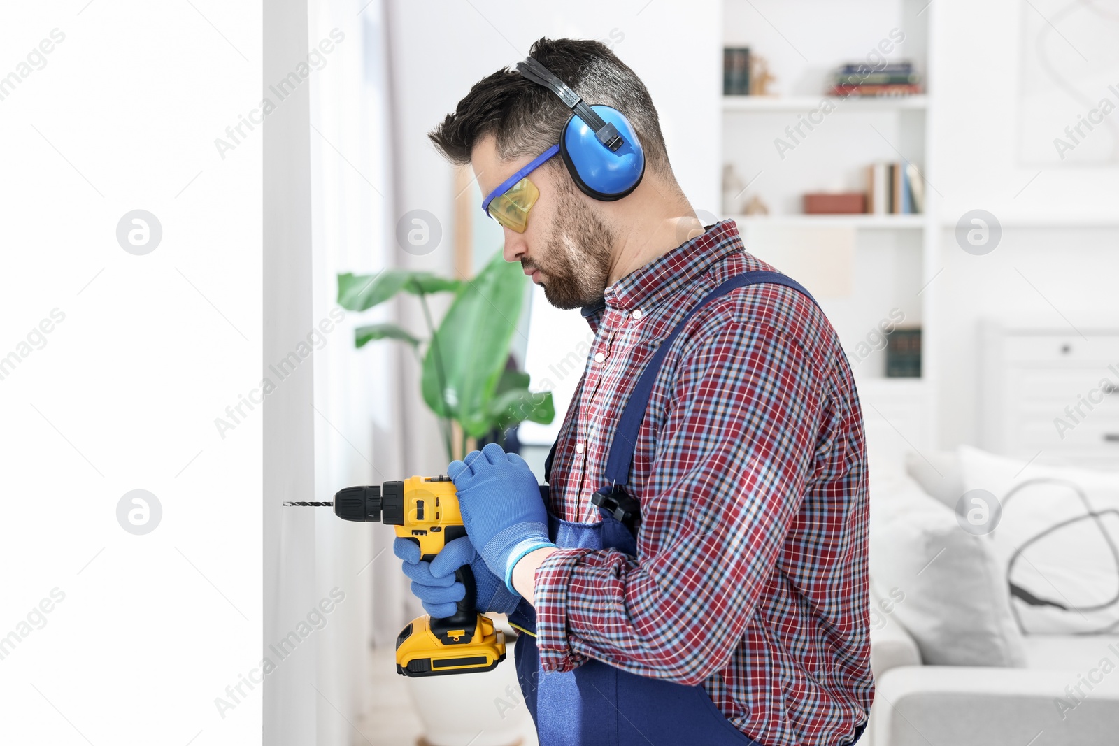 Photo of Young worker in uniform using electric drill indoors