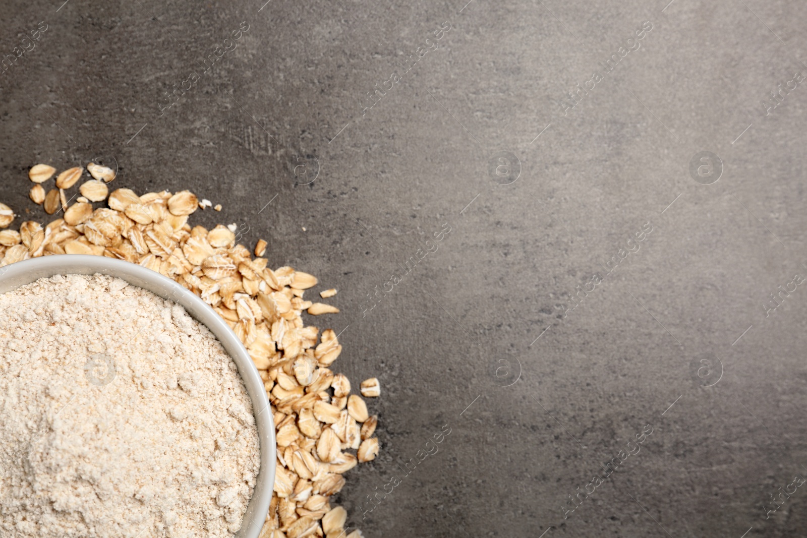 Photo of Bowl with oat flour and flakes on grey background, top view. Space for text