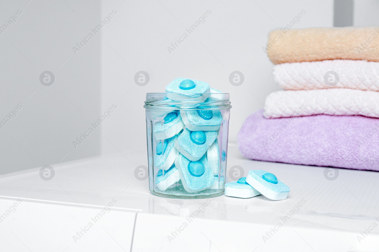 Photo of Jar with water softener tablets near stacked towels on washing machine