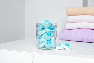 Photo of Jar with water softener tablets near stacked towels on washing machine