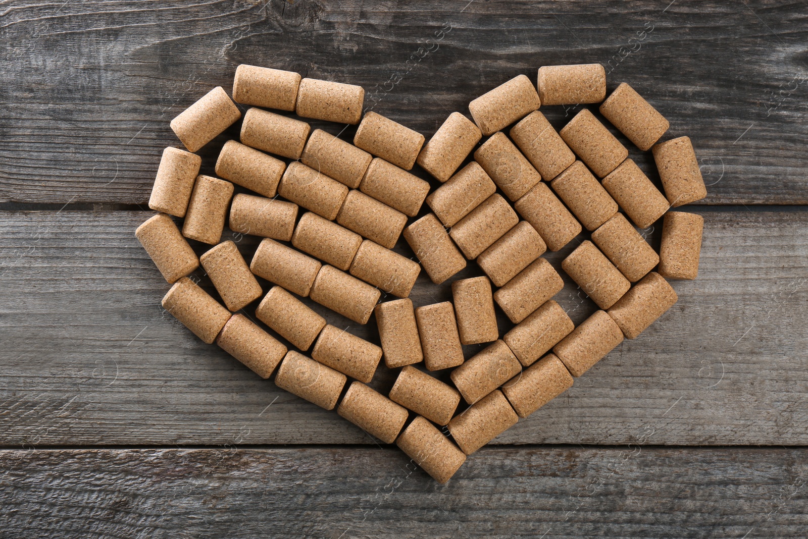 Photo of Heart made of wine bottle corks on wooden table, top view