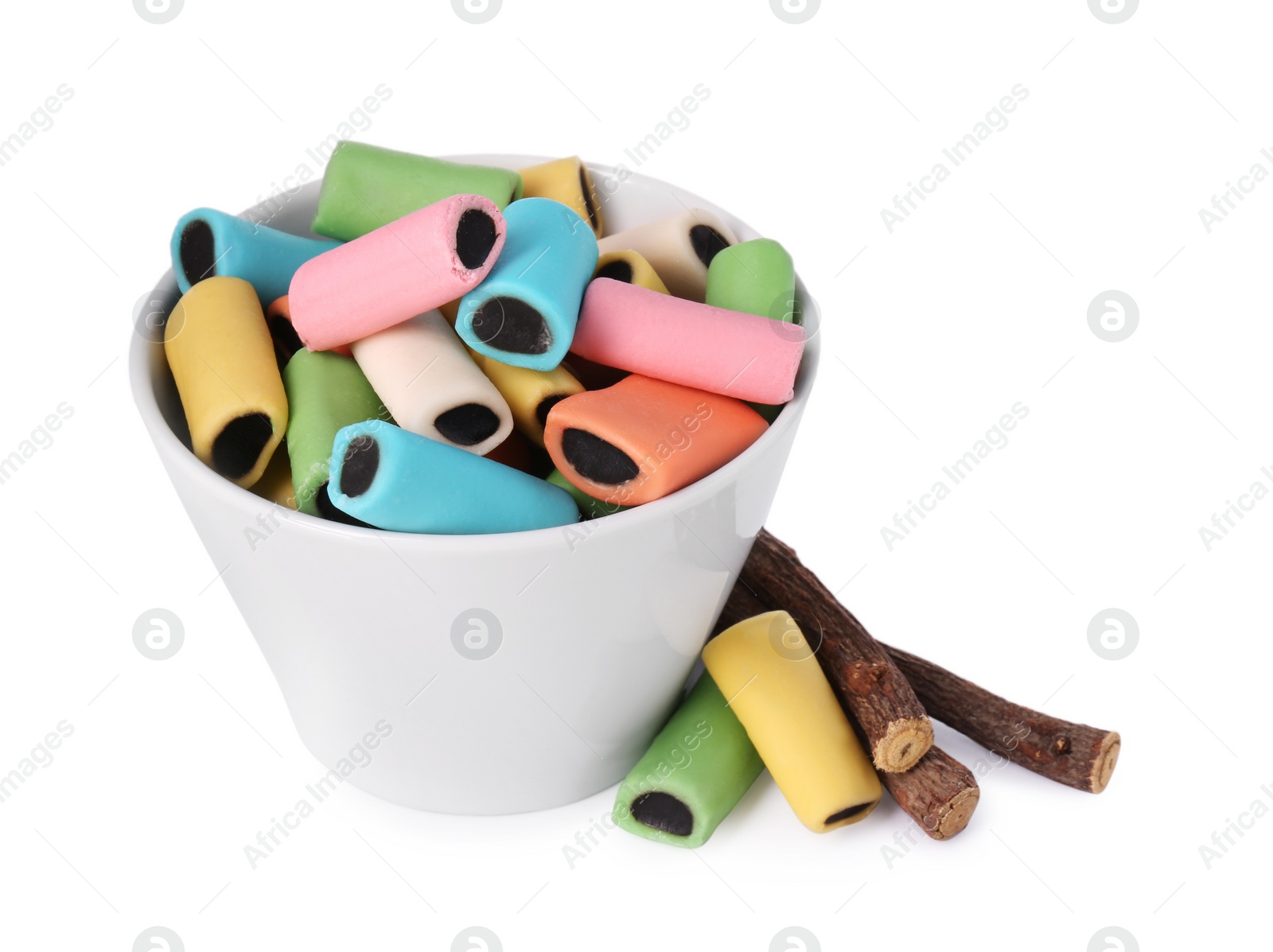 Photo of Bowl with many tasty candies and dried sticks of liquorice root isolated on white