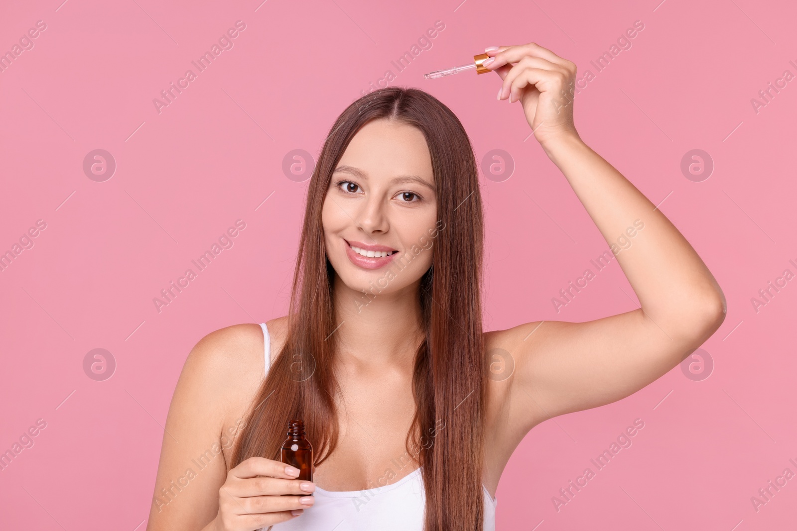 Photo of Beautiful woman applying serum onto hair on pink background