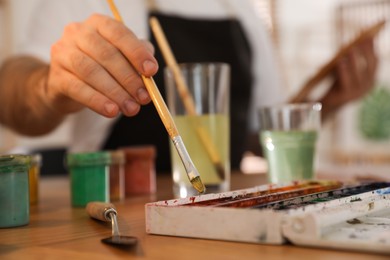 Photo of Man painting with brush at table, closeup. Young artist