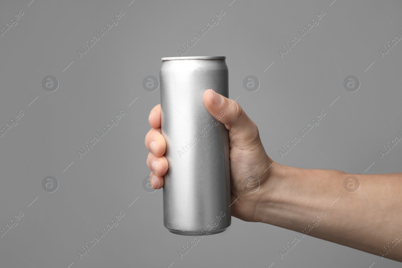 Photo of Man holding aluminum can with beverage on grey background, closeup. Space for design