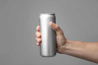 Man holding aluminum can with beverage on grey background, closeup. Space for design