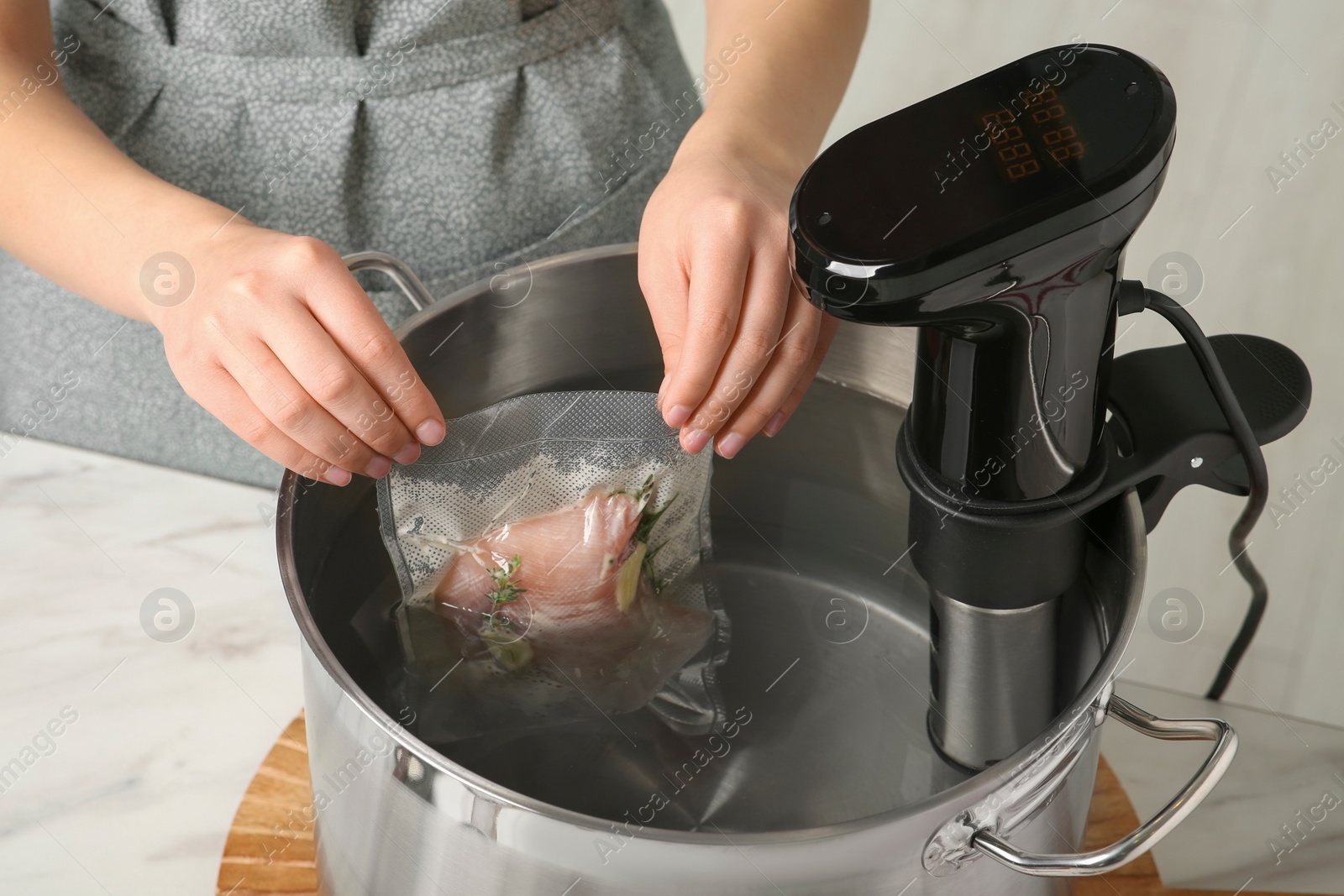 Photo of Woman putting vacuum packed meat into pot in kitchen, closeup. Thermal immersion circulator for sous vide cooking