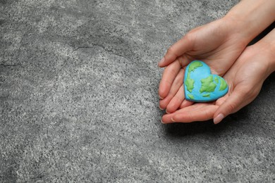 Photo of Happy Earth Day. Woman with heart shaped plasticine planet at grey table, top view and space for text