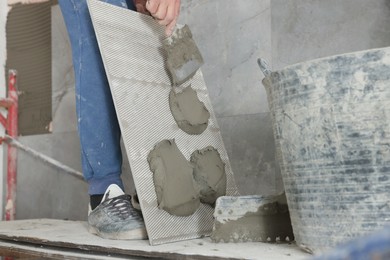 Photo of Worker applying cement on wall tile for installation indoors, closeup