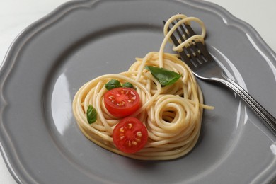 Photo of Heart made of tasty spaghetti, fork, tomato and basil on table, closeup