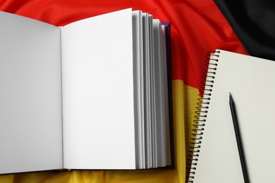 Photo of Learning foreign language. Open book, notebook and pen on flag of Germany, top view