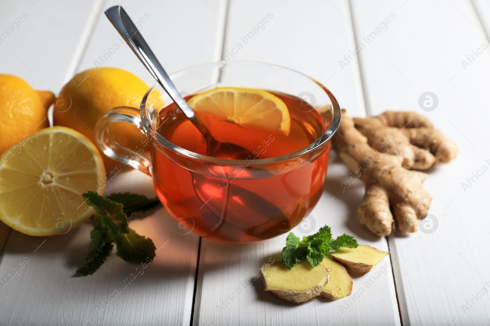 Photo of Cup of delicious ginger tea and ingredients on white wooden table, closeup