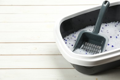 Photo of Cat litter tray with filler and scoop on white wooden floor, closeup. Space for text