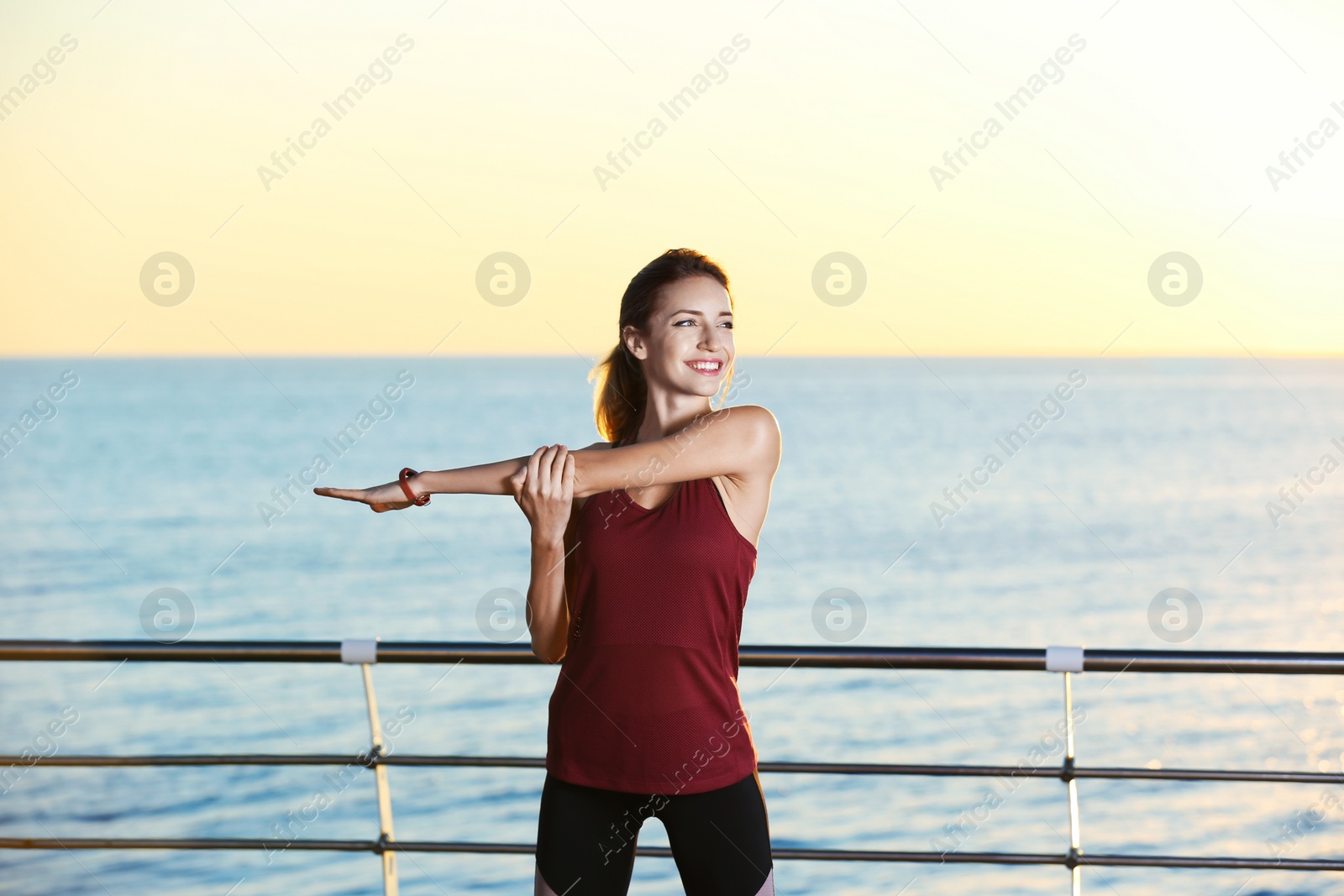 Photo of Young woman doing fitness exercises on pier in morning