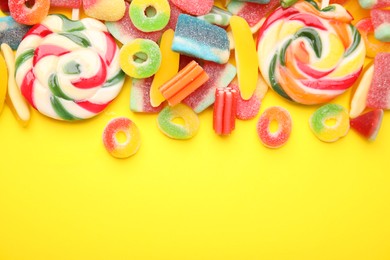 Photo of Many different jelly candies and lollipops on yellow background, flat lay. Space for text
