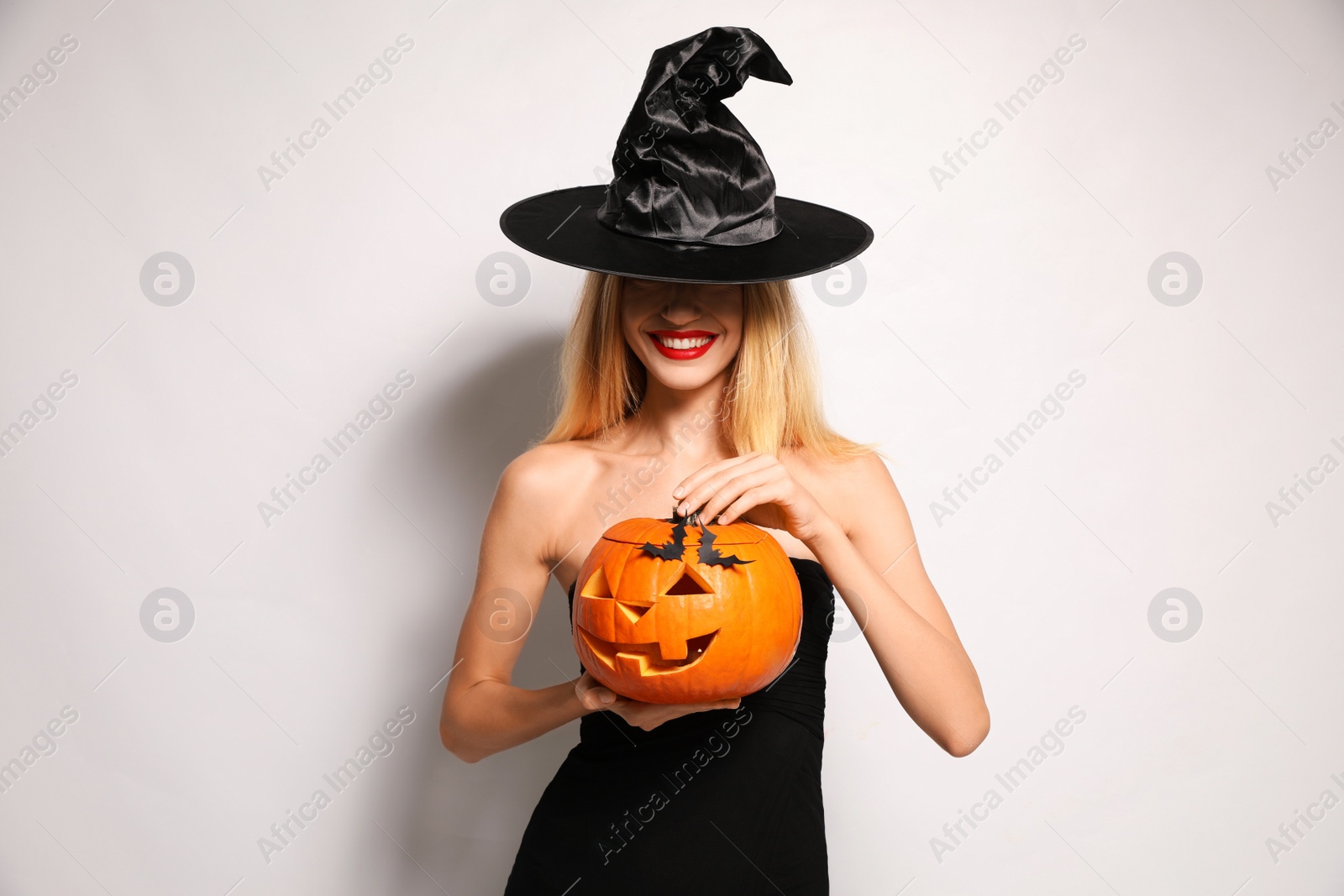 Photo of Beautiful woman in witch costume with jack o'lantern on white background. Halloween party