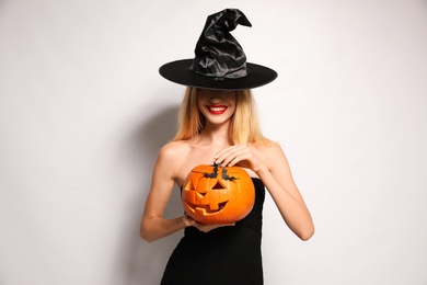 Photo of Beautiful woman in witch costume with jack o'lantern on white background. Halloween party