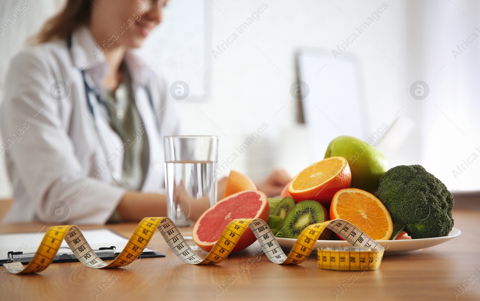 Photo of Healthy products, measuring tape and blurred nutritionist on background