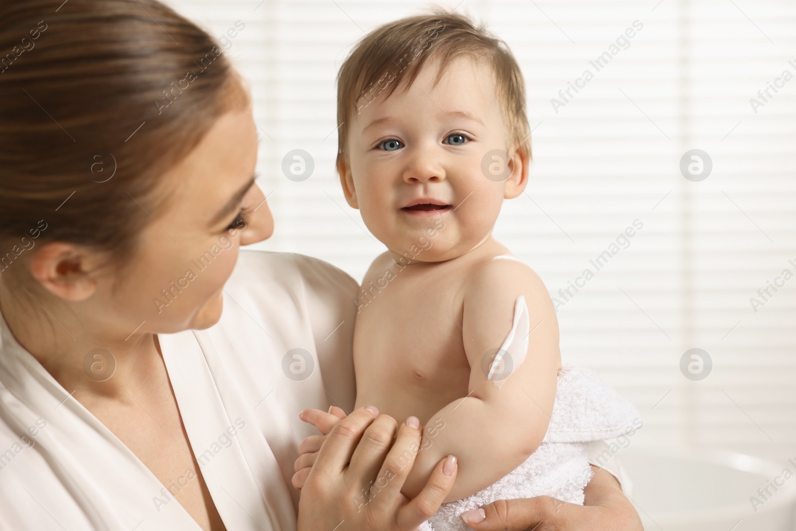 Photo of Happy mother holding her baby with body cream on skin at home