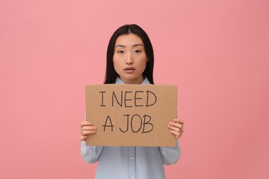Unemployed Asian woman holding sign with phrase I Need A Job on pink background