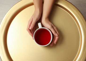 Woman with cup of black tea at golden table indoors, top view