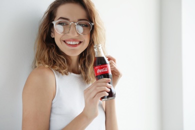 MYKOLAIV, UKRAINE - NOVEMBER 28, 2018: Young woman with bottle of Coca-Cola indoors. Space for text