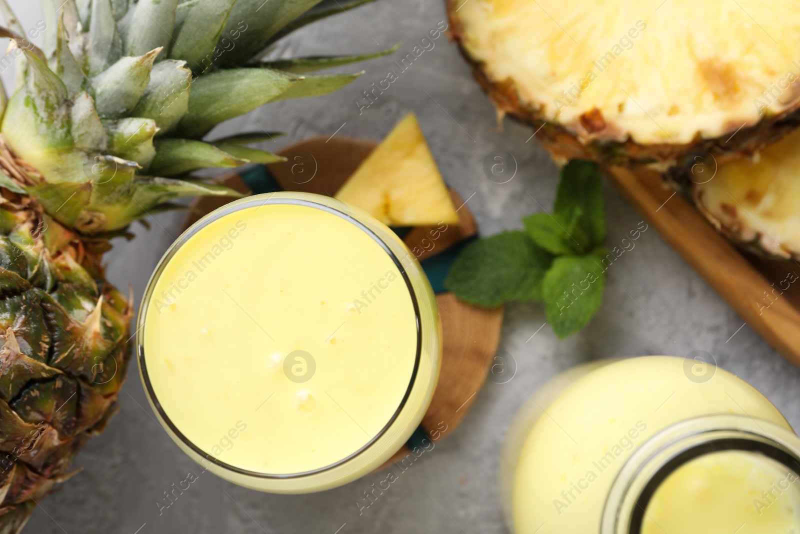 Photo of Tasty pineapple smoothie, mint and fruit on grey textured table, flat lay