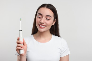 Photo of Happy young woman holding electric toothbrush on white background