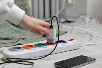 Photo of Woman putting charger into extension cord on white floor, closeup