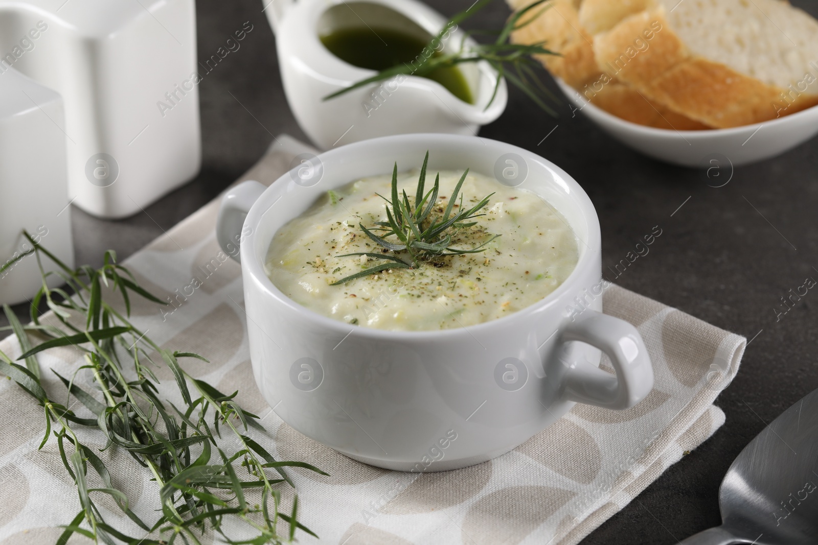Photo of Delicious cream soup with tarragon, spices and potato in bowl on dark table