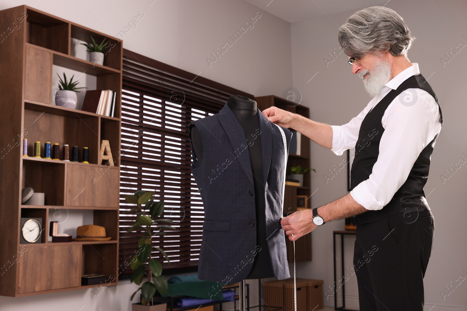 Photo of Professional tailor with measuring tape working in atelier, space for text