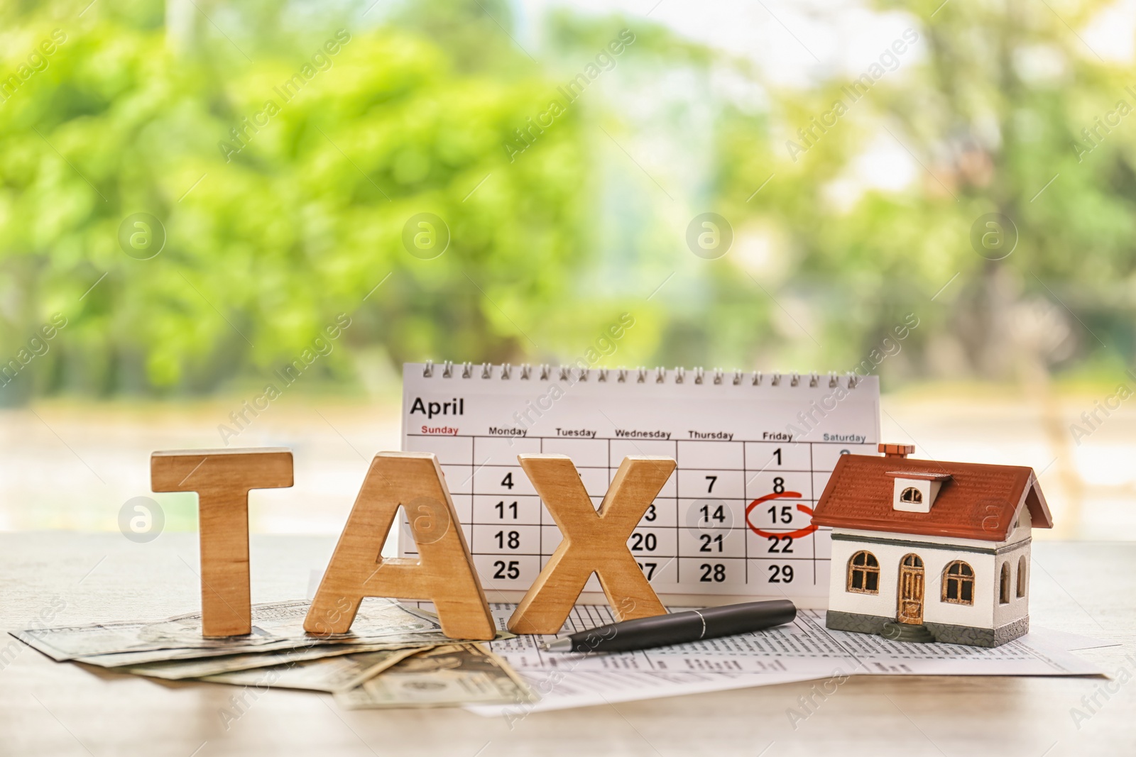 Photo of Word TAX, calendar and model of house on table