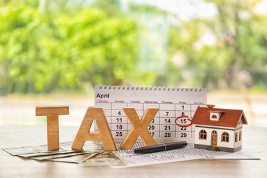 Photo of Word TAX, calendar and model of house on table