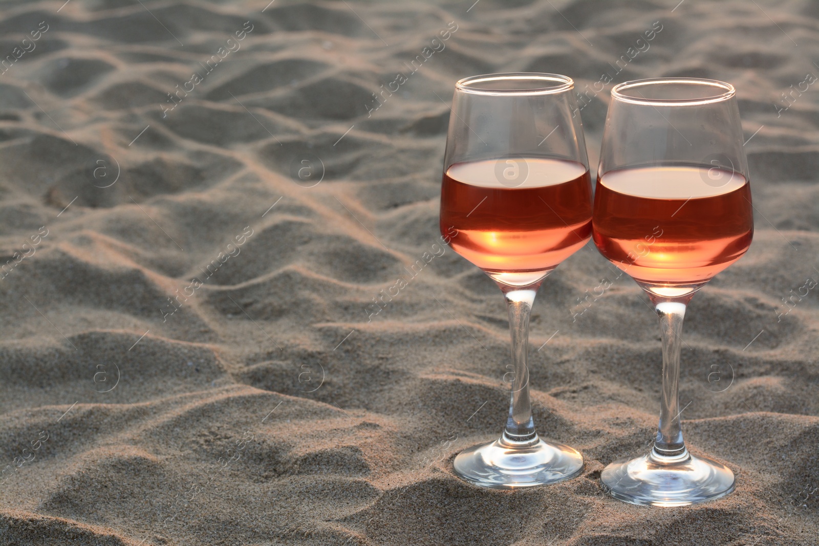 Photo of Glasses of tasty rose wine on sand, space for text