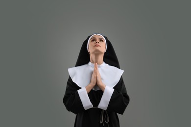 Photo of Nun with clasped hands praying to God on grey background